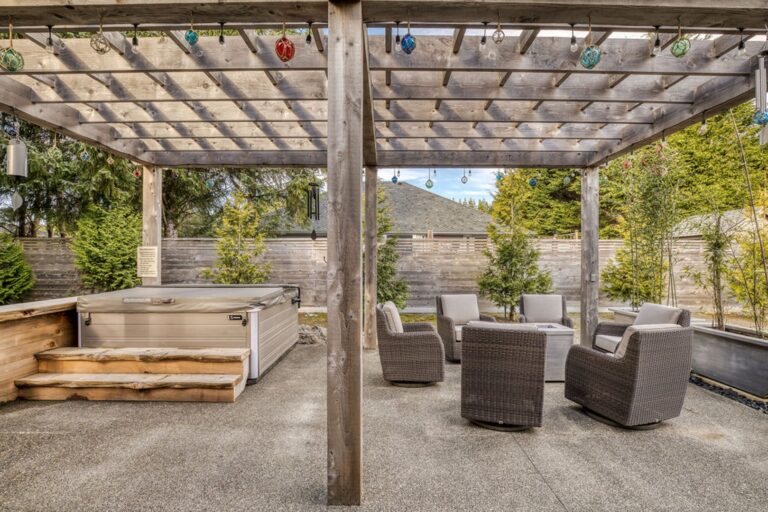 Covered outdoor area with a hot tub, fire table, and cushioned swivel chairs.