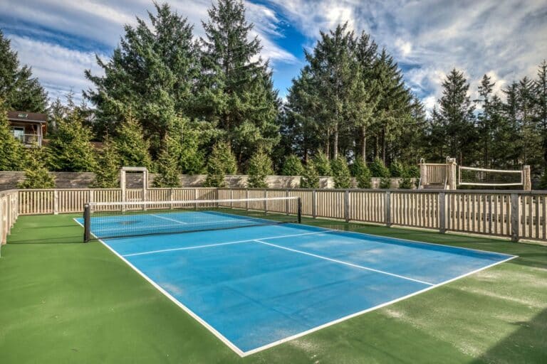 Blue and green fenced pickleball court surrounded by evergreen trees.